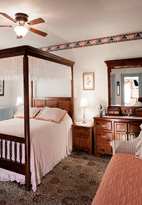 Brown canopy bed with beige bedspread and lace canopy in room with rose colored daybed on right side