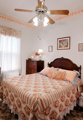 Queen sized bed with peach and white coverlet and ceiling fan above